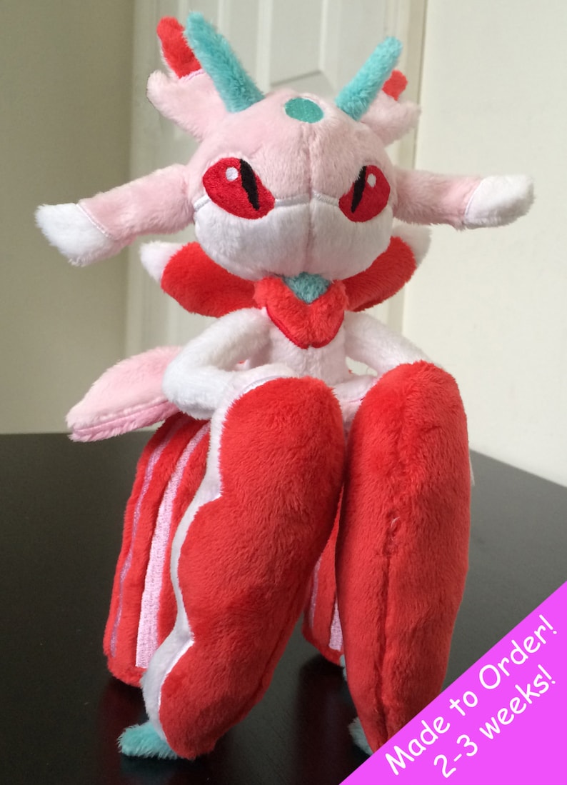 May include: Pink and red plush toy with a teal and white design. The toy has large red eyes and a teal and white crown. The toy is sitting on a black surface. Made to Order! 2-3 weeks!