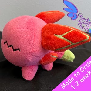 May include: Pink plush toy with red and gold wings. The toy has a black zig-zag pattern on its belly. The toy is made to order and takes 1-2 weeks to ship. "Guardian Earth Plus" is written on the background.