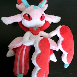 May include: A pink and red plush toy with a white face and red eyes. The toy has a long, flowing tail and a large, fluffy head.