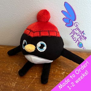 Puede incluir: Juguete de peluche de ping&uuml;ino blanco y negro con un gorro de punto rojo con un pomp&oacute;n blanco. El juguete tiene ojos bordados y un pico amarillo. El texto "Made to Order! 1-2 weeks!" es visible en la imagen.