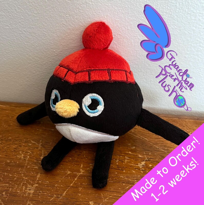 Puede incluir: Juguete de peluche de ping&uuml;ino blanco y negro con un gorro de punto rojo con un pomp&oacute;n blanco. El juguete tiene ojos bordados y un pico amarillo. El texto "Made to Order! 1-2 weeks!" es visible en la imagen.