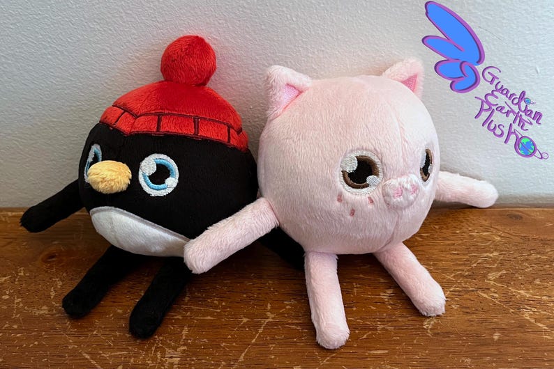 Puede incluir: Dos peluches, un ping&uuml;ino blanco y negro con un gorro rojo y un cerdo rosa con ojos marrones. Los juguetes est&aacute;n sentados sobre una superficie de madera. El texto "Guardian Earth Plush" es visible en el fondo.