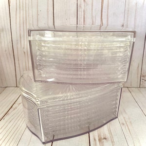 May include: Two clear, plastic, heart-shaped containers with lids. The containers are stacked on top of each other, with the bottom container slightly larger than the top one. The containers are empty and appear to be new.