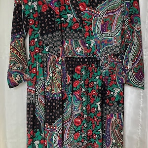 Może przedstawiać: Sukienka w stylu vintage z czarnym tłem i kolorowym wzorem paisley i kwiatowym. Sukienka ma czerwone, zielone i fioletowe akcenty, dekolt w serek i długie rękawy. Sukienka ma białą poszetkę.