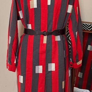 Könnte beinhalten: Ein langärmeliges rot-schwarz gestreiftes Kleid mit weißem Kragen und Gürtel. Das Kleid hat ein geometrisches Muster aus Quadraten in verschiedenen Farben.