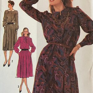May include: A woman models a paisley print dress with long sleeves, a brown belt, and a gold necklace. The image is a vintage sewing pattern, with illustrations of other dress designs. The word "SIMPLICITY" is printed at the bottom.