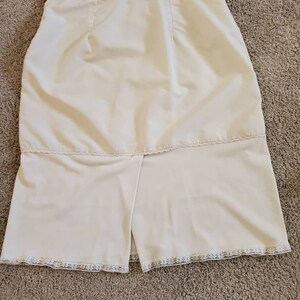 Pu&ograve; includere: Gonna vintage color crema con spacco sull'orlo. La gonna ha una vita alta e una chiusura con bottoni. L'orlo &egrave; rifinito con un delicato pizzo. Il tessuto sembra essere un materiale liscio e leggero.