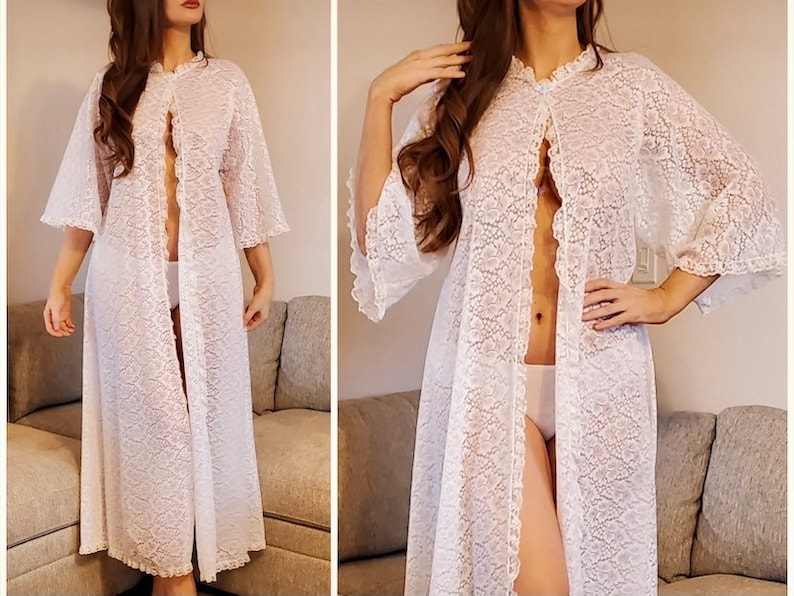 May include: A white lace robe with a floral pattern. The robe has a ruffled collar, wide sleeves, and a floor-length design. The robe is open in the front and has a delicate, feminine aesthetic.