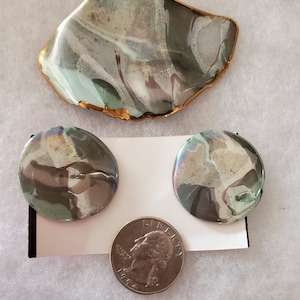 May include: A vintage jewelry set featuring a brooch and two matching clip-on earrings. The brooch is an irregular shape with a gold-colored trim. The earrings are round. All pieces have a marbled design in shades of gray, green, and white.