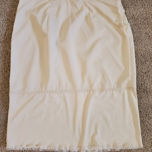 Pu&ograve; includere: Gonna color crema con taglio dritto, con delicati bordi in pizzo sull'orlo e una fascia orizzontale. La gonna ha una consistenza liscia, leggermente lucida e sembra essere realizzata in un tessuto leggero.