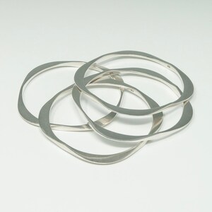 May include: Four silver bangles with a wavy, organic shape. The bangles are stacked on top of each other.