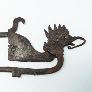 Può includere: Una chiave di metallo arrugginito a forma di drago con dettagli intricati. La chiave è progettata con un manico lungo e una testa di drago con la bocca aperta.