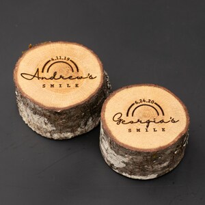 May include: Two wooden slices with engraved text and rainbow designs. The top slice reads "Andrew's Smile" with the date "4.11.19". The bottom slice reads "Georgia's Smile" with the date "6.24.20".
