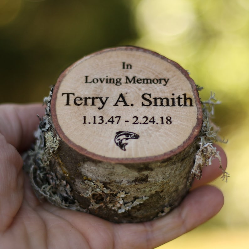 Pu&ograve; includere: Una targa commemorativa in legno con il testo "In Loving Memory Terry A. Smith 1.13.47 - 2.24.18" e una piccola silhouette di pesce.