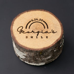May include: A wooden round slice with a rainbow and the text "Georgia's Smile" and the date "6.24.20" engraved on it.