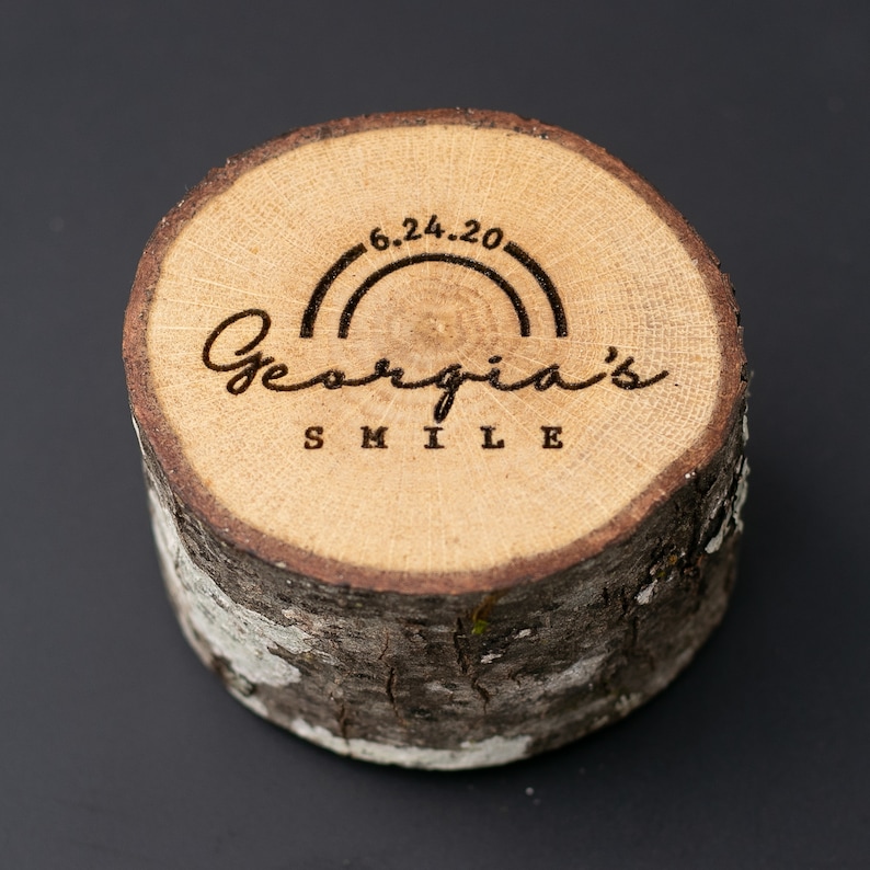 May include: A wooden round slice with a rainbow and the text "Georgia's Smile" and the date "6.24.20" engraved on it.