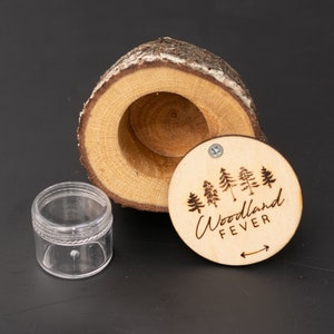 May include: A wooden box with a round lid, the lid has a design of trees and the text "Woodland Fever" with an arrow pointing to the right. The box is open and a clear plastic container is sitting next to it.