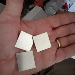 May include: Three silver metal squares, each with a slightly different shape, are held in a hand.