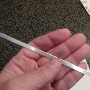 May include: A silver metal rod, approximately 10 inches long, is held in a person's hand.