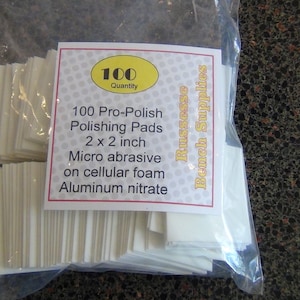 May include: A clear plastic bag containing 100 white square Pro-Polish Polishing Pads. The label reads 100 Quantity, 100 Pro-Polish Polishing Pads, 2 x 2 inch, Micro abrasive on cellular foam, Aluminum nitrate, and Russesse Bench Supplies.