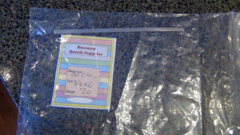 May include: A clear plastic bag with a label that says "Russwin Bench Supplies". The label has a yellow, pink, blue, and white striped background. The label also includes the following information: Metal type: 1/4" St. Steel, Size: 3 1/2" x 6, Gauge: 20.