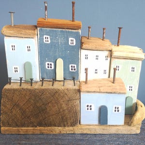 Case e cottage in legno di recupero, adagiati l&#39;uno sull&#39;altro su una base in legno di recupero, formano una scena di porto costiero dai colori marini, utilizzando legno di recupero.