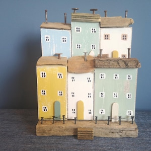 Case e cottage in legno di recupero, adagiati l&#39;uno sull&#39;altro su una base in legno di recupero, formano una scena di porto costiero dai colori marini, utilizzando legno di recupero.