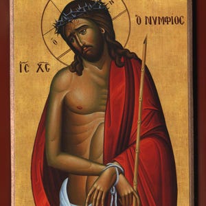 Può includere: Icona religiosa raffigurante una figura con una corona di spine, che indossa una veste rossa e tiene in mano un bastone. La figura ha un'aureola e si trova su uno sfondo dorato. L'immagine è incorniciata in un bordo di legno.