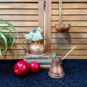 May include: A white ceramic mug with a black handle and the text "But First, Coffee" in a bold, black font. The mug is set against a blurred background, suggesting a cozy setting.