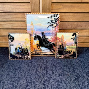 May include: Three framed silhouette art pieces depicting scenes of equestrian and carriage travel. The central piece shows a rider on a jumping horse. The other two pieces show carriages with horses. The frames have a gold and brown border.