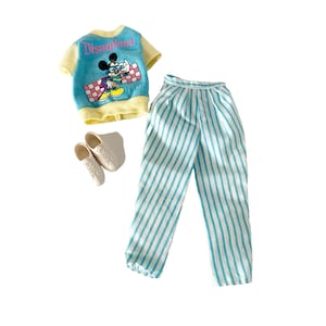 May include: A vintage doll outfit comprising a blue and yellow sweater with "Disneyland" text and a Mickey Mouse graphic. The outfit includes striped trousers and white shoes. The sweater has a crew neck and short sleeves.