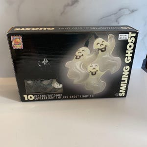 May include: A black rectangular cardboard box containing a set of 10 indoor and outdoor super bright smiling ghost lights. The packaging features a graphic of three white ghost-shaped light covers with smiling faces and the text SMILING GHOST.