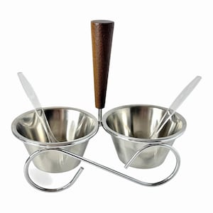 May include: A condiment server featuring two stainless steel bowls held in a chrome wire frame with a central dark wood handle. Two clear plastic spoons are placed inside the bowls. The structure is supported by a curved metal base.
