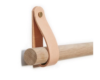 Puede incluir: Un toallero de madera con una correa de cuero y herrajes de latón. La barra está montada en una pared.