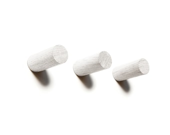 May include: Three white wooden hooks mounted on a white wall. The hooks are cylindrical in shape and are arranged in a row.