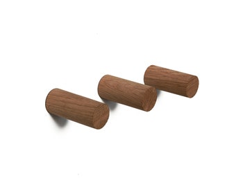 May include: Three wooden wall hooks in a light brown color. The hooks are cylindrical in shape and are mounted on a white wall.