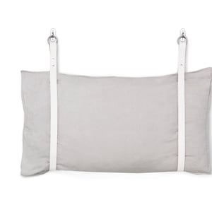 May include: A light grey linen pillow with white leather straps and silver metal hooks. The pillow is hanging from the straps.