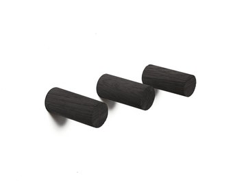 May include: Three black wooden wall hooks, each with a cylindrical shape. The hooks are mounted on a white wall.