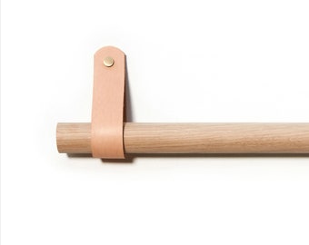 Puede incluir: Una barra de madera con una correa de cuero unida a un extremo. La correa tiene un botón de latón.