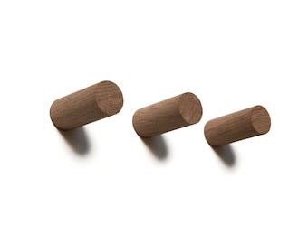 May include: Three wooden wall hooks in a light brown color. The hooks are cylindrical in shape and are mounted on a white wall.