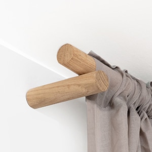 May include: Close-up of a wooden curtain rod with a gray curtain hanging from it. The rod is mounted to a white wall.