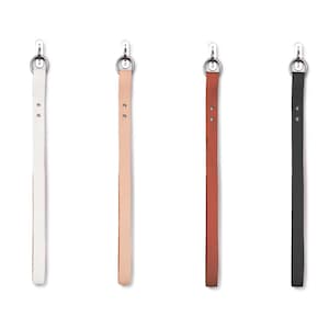May include: Four leather straps with metal rings at the top, hanging from hooks. The straps are white, light brown, dark brown, and black.