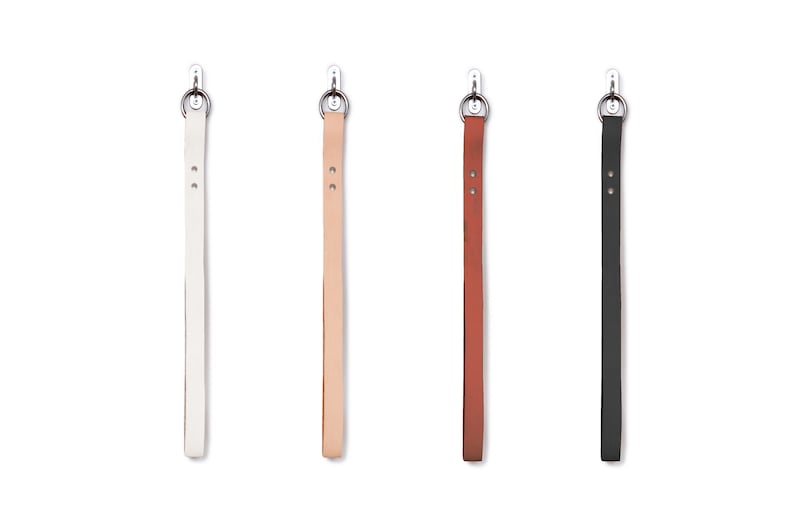 May include: Four leather straps with metal rings at the top, hanging from hooks. The straps are white, light brown, dark brown, and black.