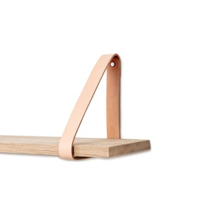 Op de afbeelding: Een lichte houten plank met een lichtbruine leren band die aan de onderkant is bevestigd. De plank is aan een muur gemonteerd.