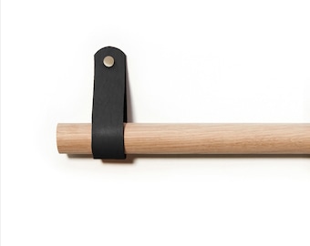 Puede incluir: Una barra de madera con una correa de cuero negro unida a un extremo. La correa tiene un botón de metal.
