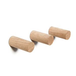May include: Three wooden wall hooks in a light brown color. The hooks are cylindrical in shape and have a smooth, natural finish.