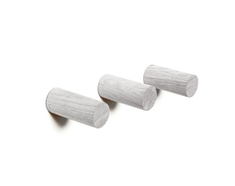 May include: Three white wooden wall hooks in a row. The hooks are cylindrical and have a rough, textured surface.