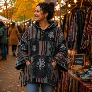 May include: A black hooded pullover with a front kangaroo pocket, featuring vertical multicoloured striped panels and white floral embroidery. The garment has a drawstring hood, long sleeves, and side ties at the hem, showcasing a textured finish.