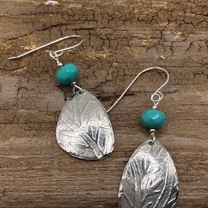 May include: A pair of silver dangle earrings with a turquoise bead and a leaf design.