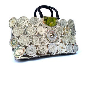 May include: A white handbag made from rolled up newspaper with a black handle and gold accents. The bag has a gold metal plate with the word "Anya" on it.